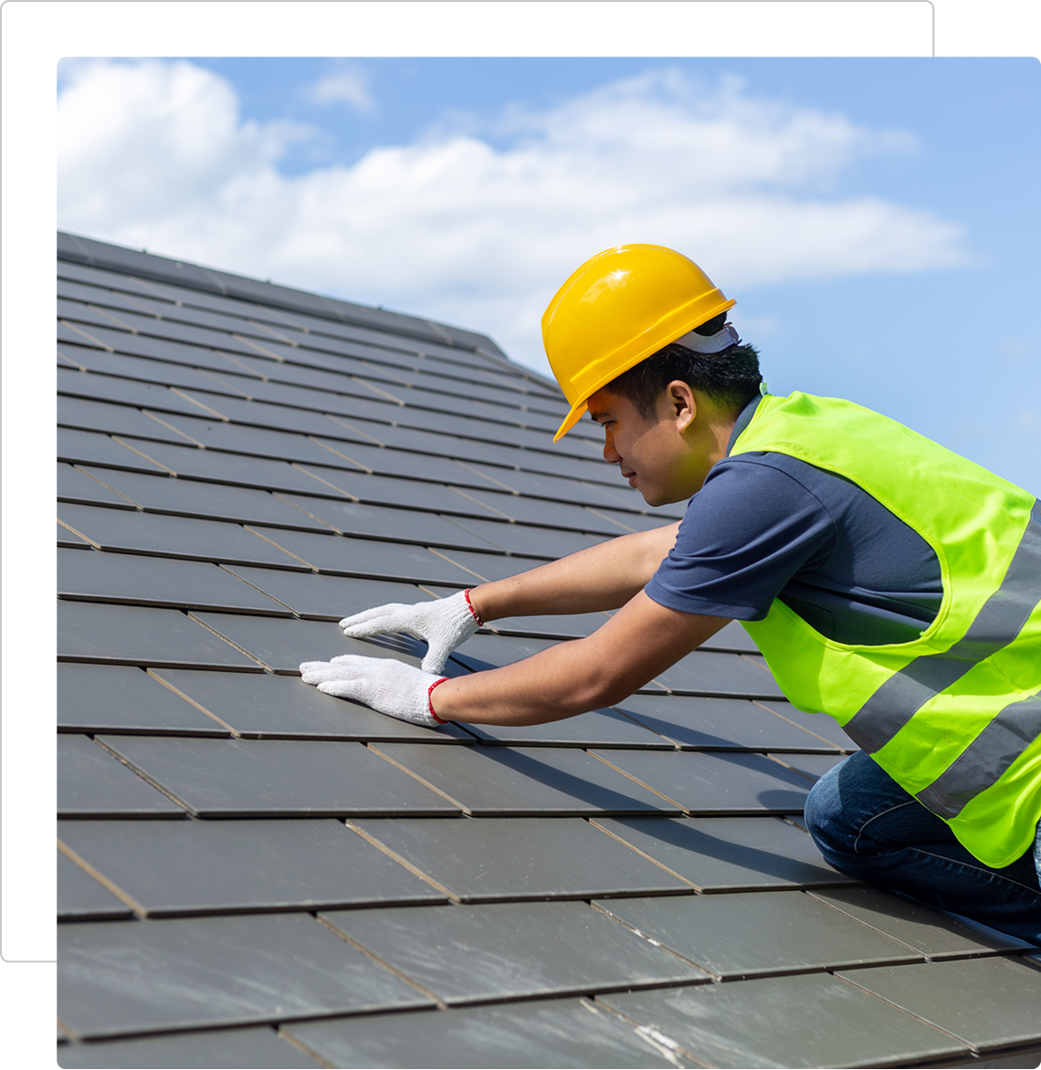 Construction worker installing roof tiles under a blue sky.