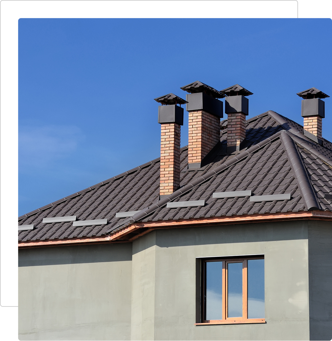 Modern house roof with brick chimneys under clear blue sky.